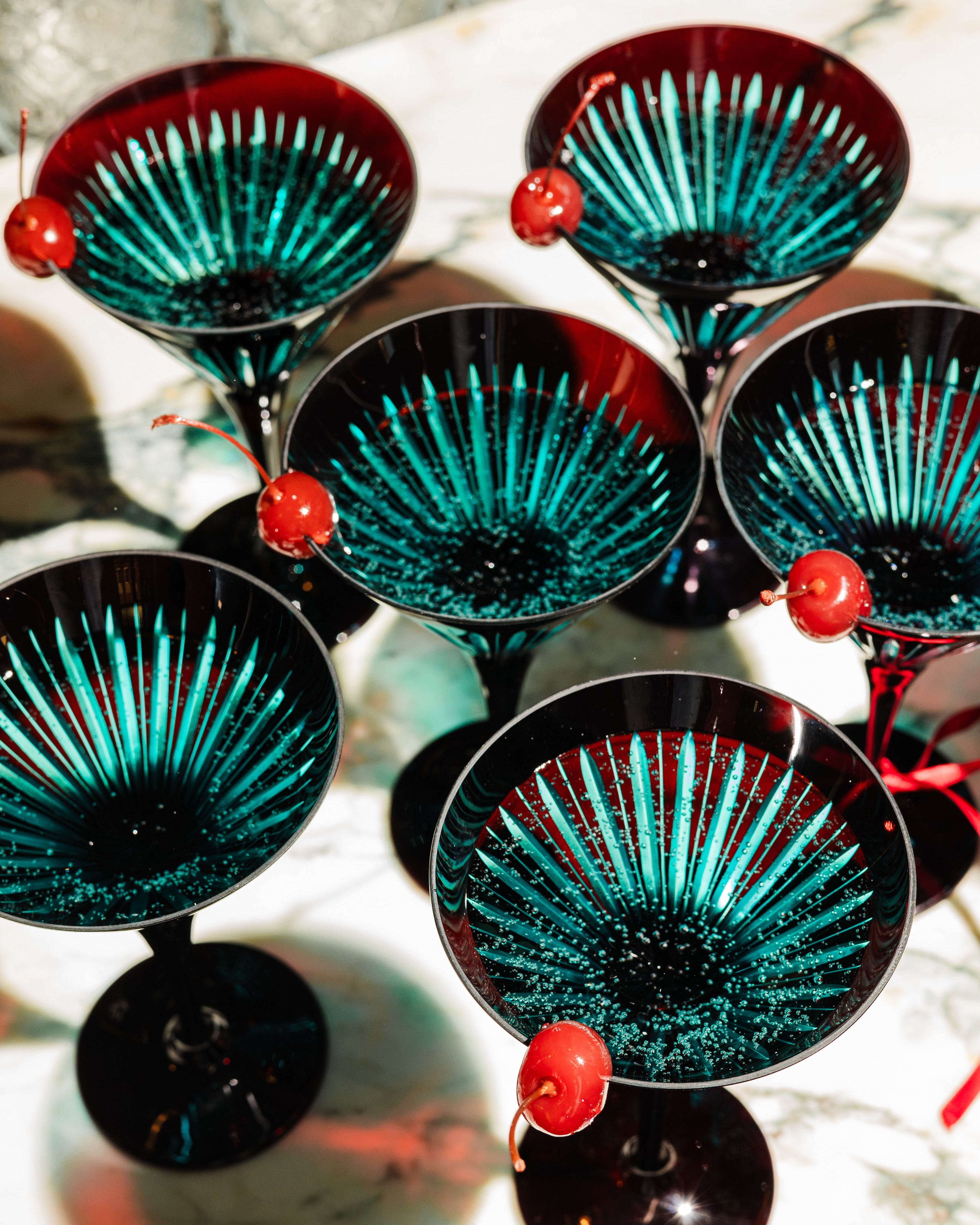 Set of six blue cocktail glasses with red cherries on a white surface