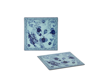 Set of 2 square porcelain placemats in Iris from the Oriente Italiano collection, featuring a blue floral pattern on an iris blue background with gold threading accents.