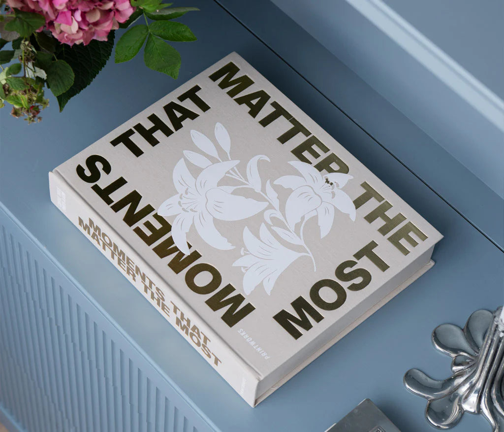 Moments that Matter the Most Coffee Table Photo Album with a beige cloth cover and gold foiled text. Includes 30 white photo paper pages for two 10x15 cm photos per page, made with FSC-certified materials and a black metal binder.