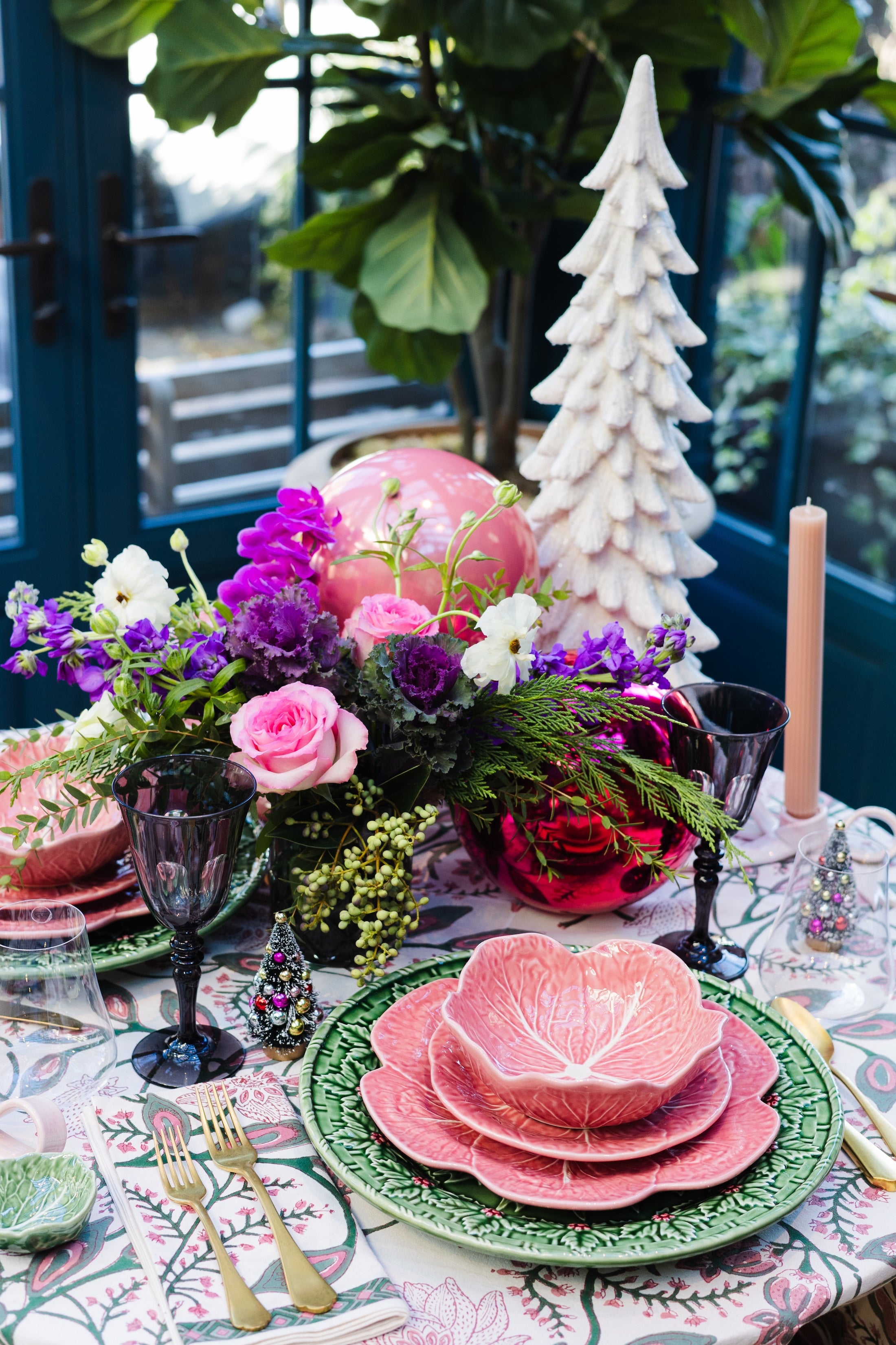 Decorative table setting with pink floral centerpieces, green plates, and a white ceramic Christmas tree.